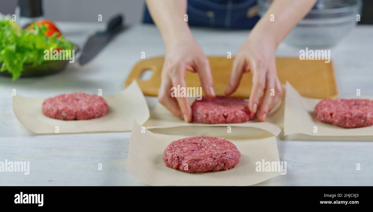 Mano della donna che forma una carne di manzo per una festa di hamburger. Porzionamento carne macinata. Hamburger fatti in casa. Fare il cibo a casa. Foto Stock