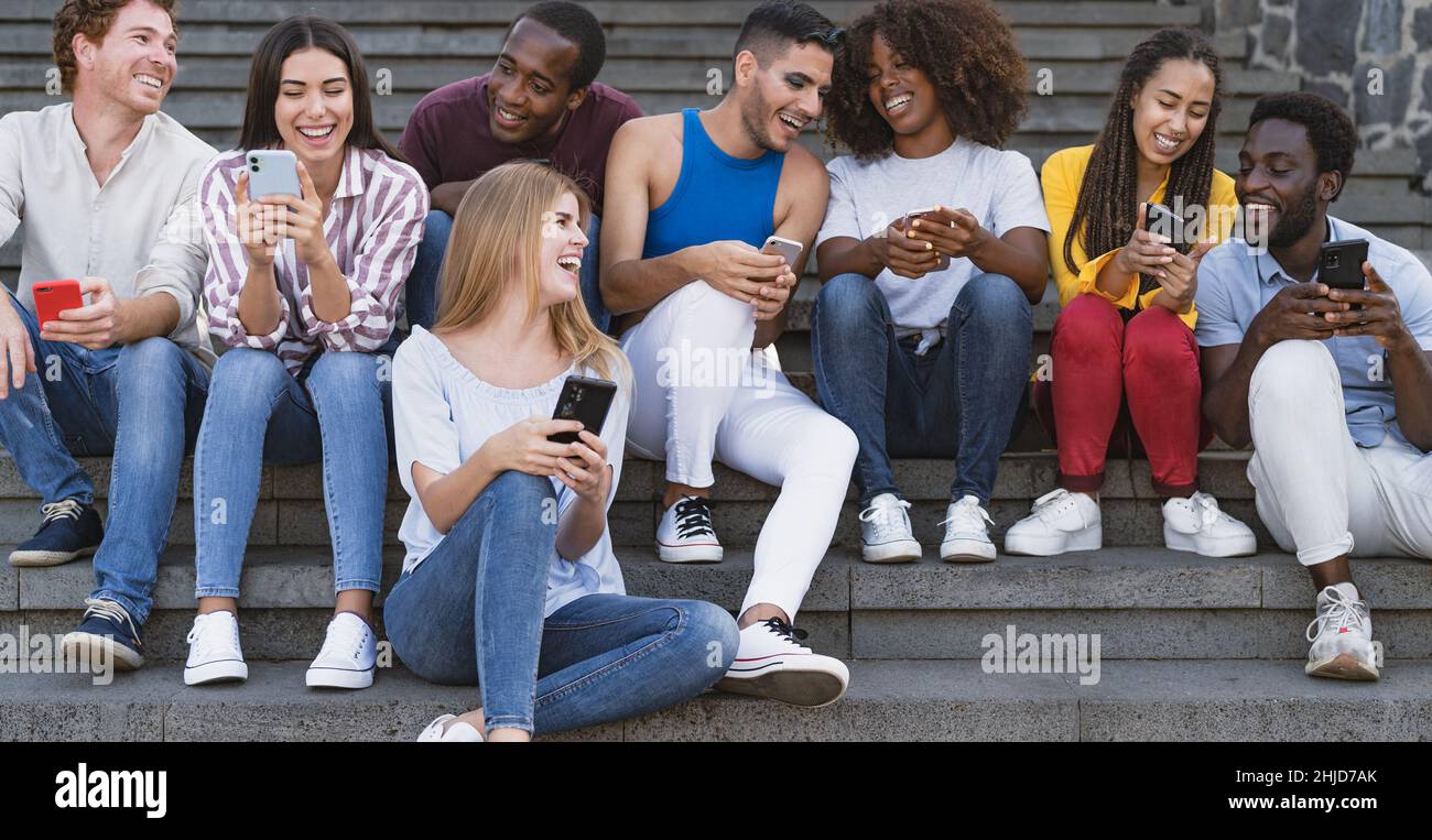 Giovane gruppo di amici multirazziale che usa lo smartphone mobile seduto su scale fuori dall'università - concetto di stile di vita millenario della gioventù Foto Stock