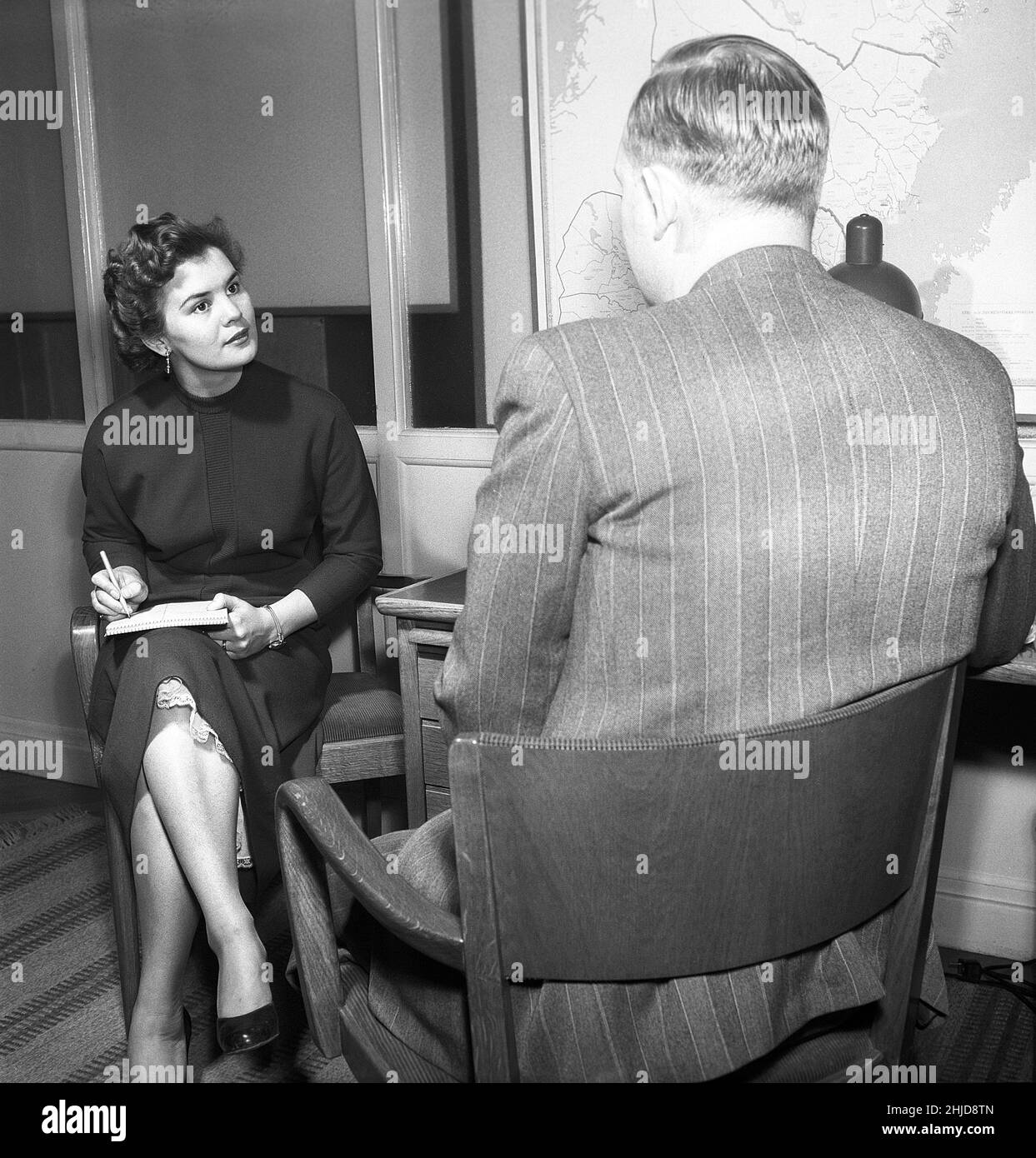 Ufficio ragazza nel 1950s. Una donna è seduta con un taccuino nel suo giro che scrive le note di che cosa l'uomo dice, possibilmente una lettera che più successivamente scriverà. Avere un segretario era più comune in passato allora oggi. È ben vestita e dà un'impressione seria. Ha una visibile sotto la gonna. Svezia 1954.Photo Kristoffersson BO25-2 Foto Stock