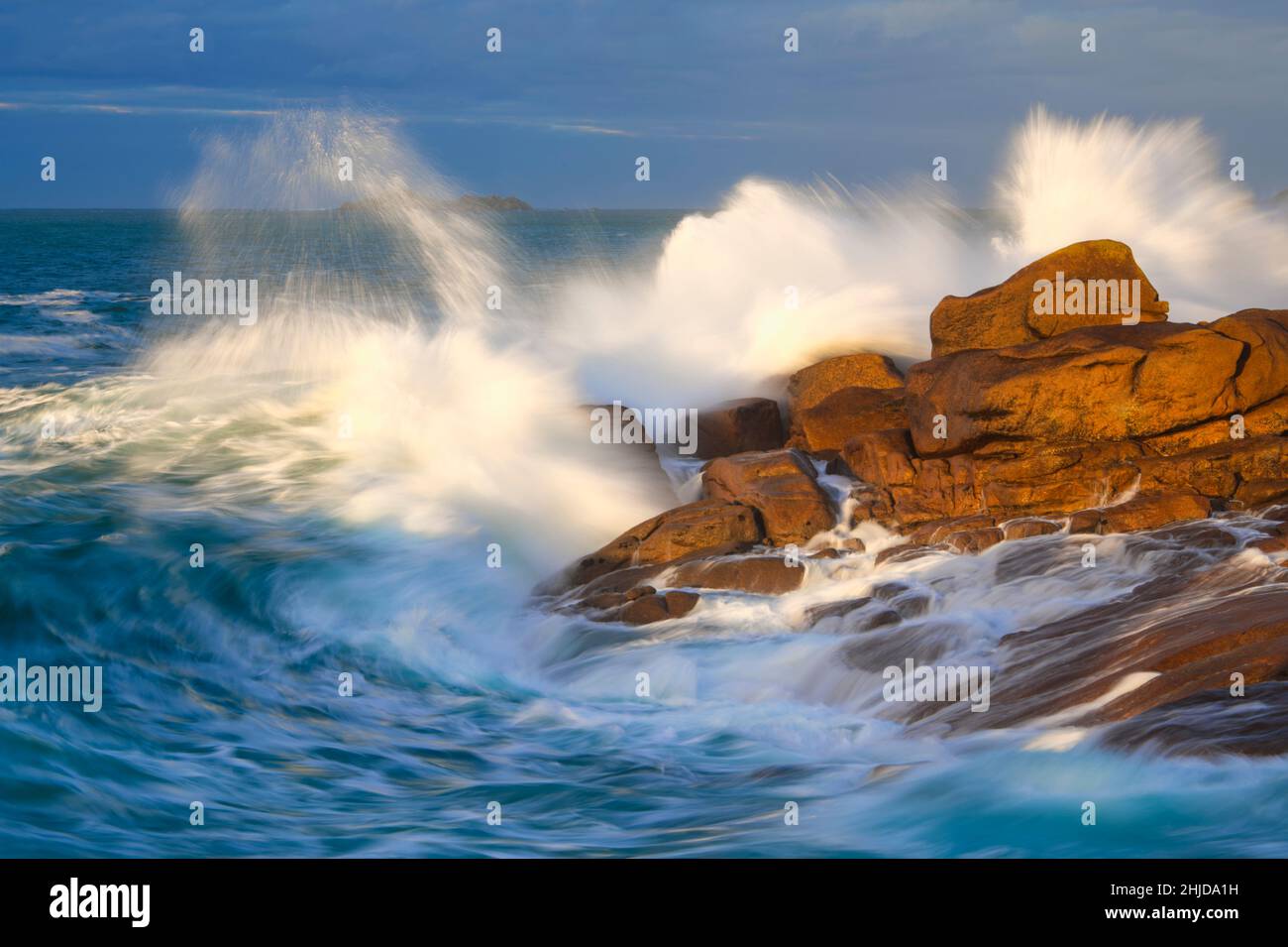 Le onde dell'oceano si infrangono sulle grandi rocce rosse della costa Foto Stock