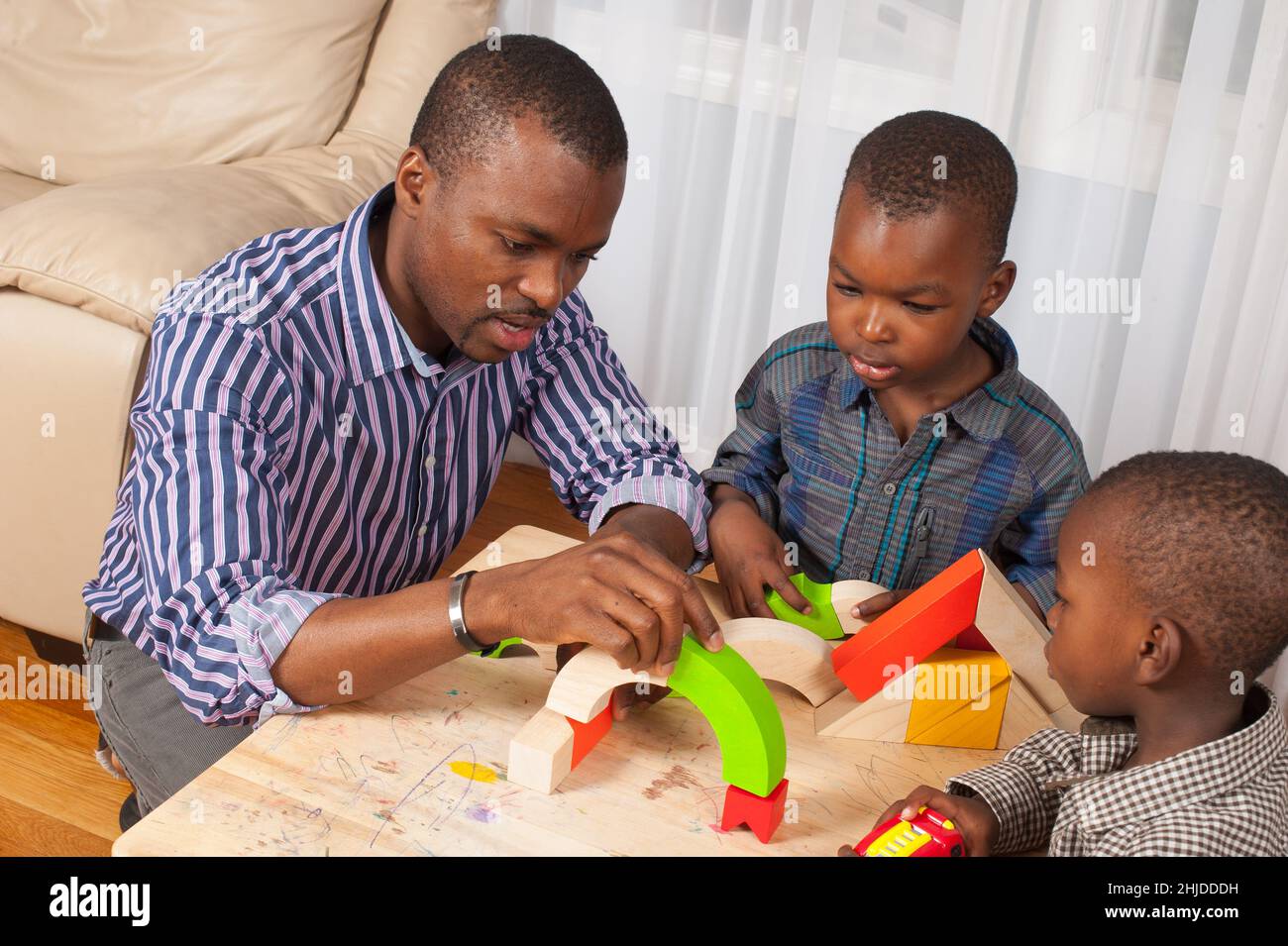 il ragazzo di 2 anni guarda il padre e il fratello di 4 anni, aspettando che costruisca un tunnel per il camion che sta tenendo Foto Stock