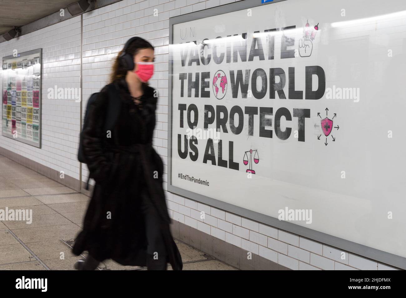 La donna in maschera rossa cammina oltre il poster sul cartellone mostrando 'vaccino il mondo per proteggerci tutti', Inghilterra Regno Unito auto isolamento regole che stanno per finire presto Foto Stock