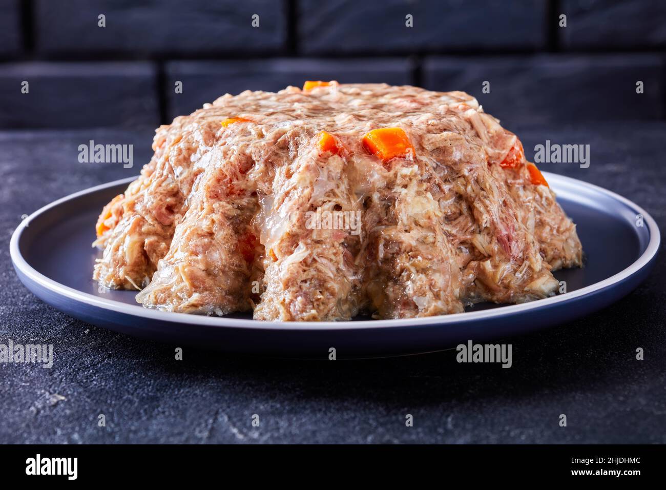 carne di maiale e pollo aspica, gelata carne cotta lenta su un piatto su un tavolo di cemento con una parete di mattoni neri sullo sfondo, primo piano Foto Stock