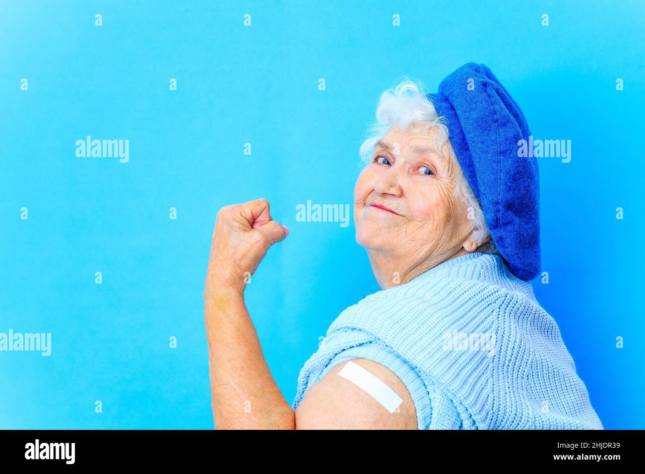 bella donna in pensione in beretto blu e caldo pullover guardando la macchina fotografica e il sorriso in sfondo blu parete in studio Foto Stock