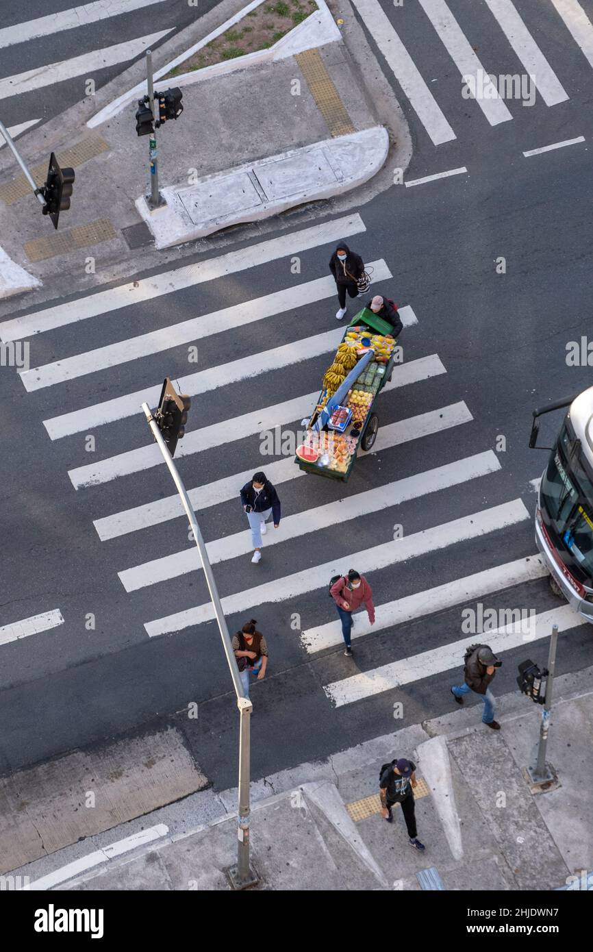 America Latina. Vista elevata dei pedoni su un cross walk in Brasile. Venditore che spinge un carrello di frutta. Zebra attraversando un viale urbano molto trafficato. Foto Stock