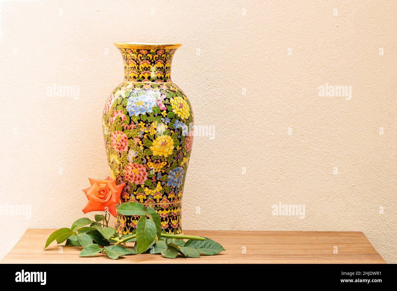 Bella Benjarong vaso con rosa rossa e foglia verde su tavola di legno. Il prezioso souvenir thailandese chiamato Benjarong è in porcellana design in cinque colori patt Foto Stock