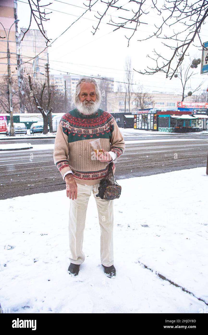 Ucraini. L'uomo anziano ucraino in un maglione in un gelido giorno di gennaio sta rimanendo sulla strada a Kiev, con un vetro di plastica della lager nella mano sinistra. Foto Stock