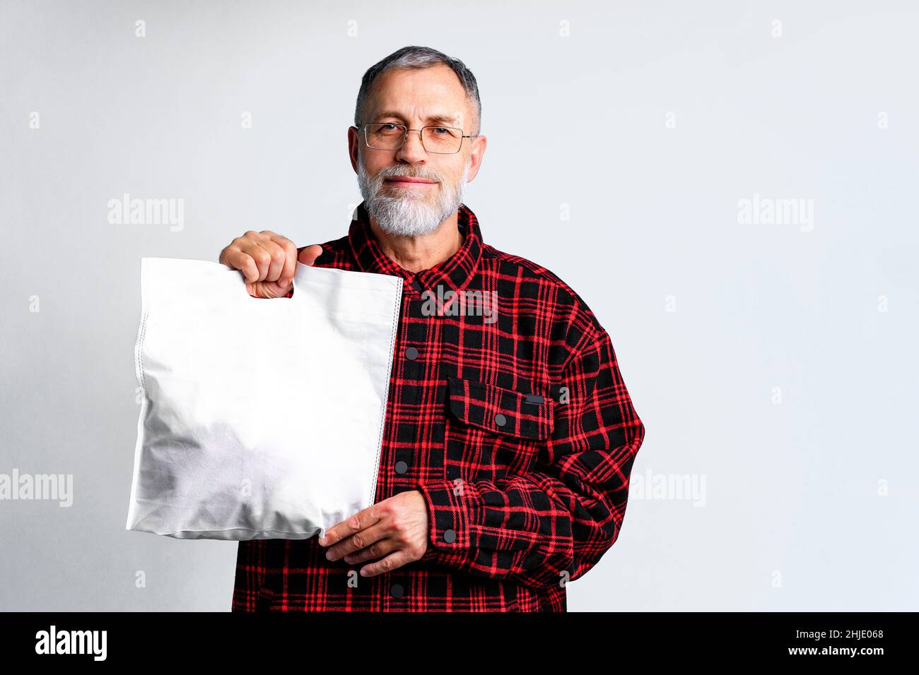 l'uomo maturo tiene in mano la borsa ecologica in tessuto bianco su sfondo bianco Foto Stock