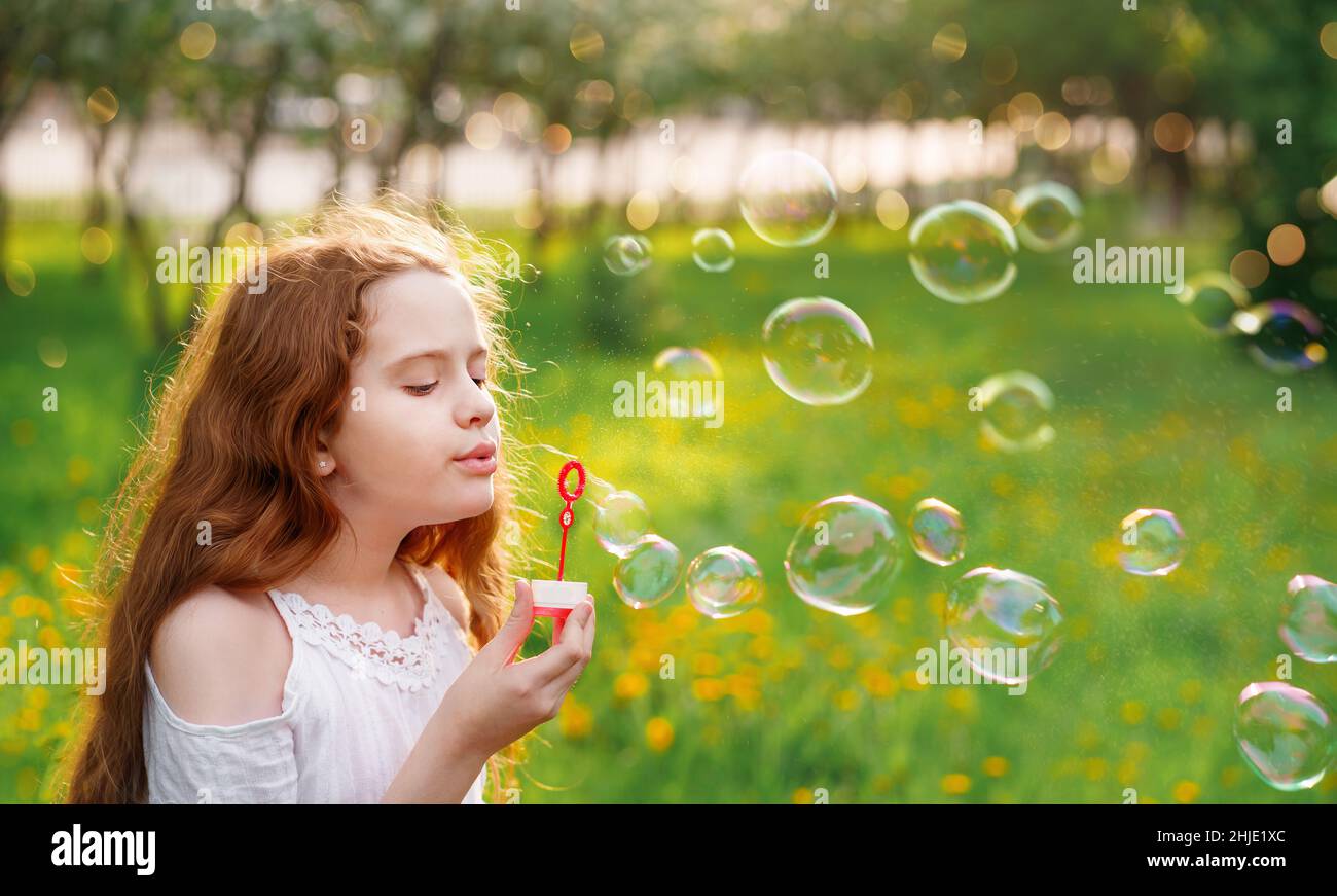 Bella ragazza soffiando bolle di sapone nel parco estivo. Concetto di infanzia felice. Foto Stock
