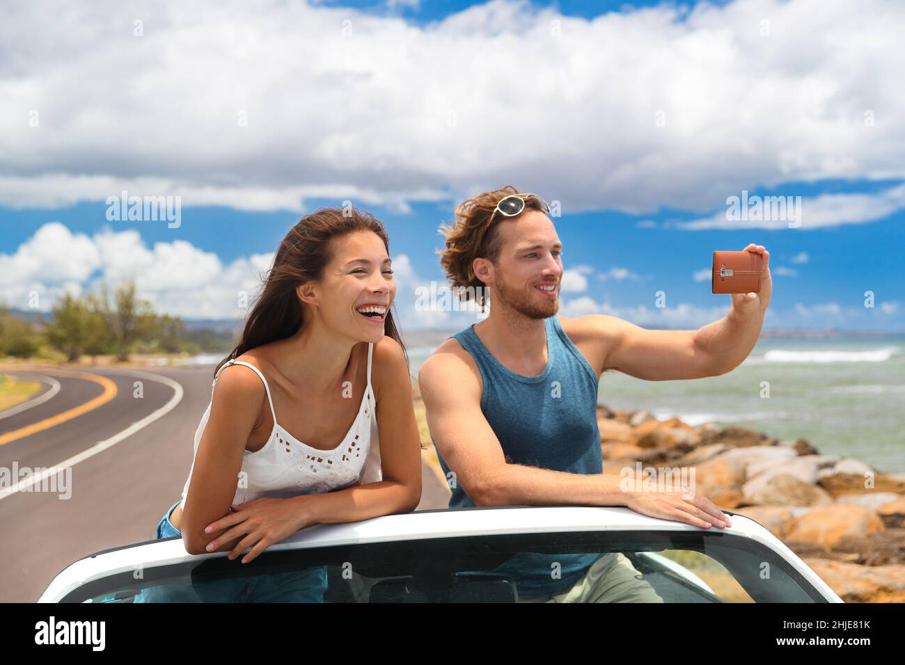 Viaggio di strada vacanza sport auto persone fotografando il paesaggio delle Hawaii durante il viaggio estivo. Coppia di turisti che scattano foto con lo smartphone Foto Stock