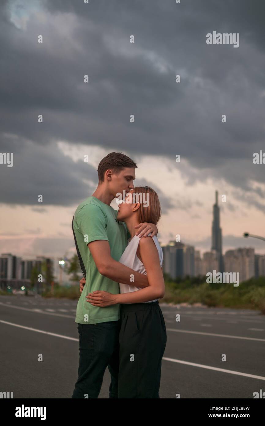 Bella giovane coppia in piedi sulla strada nella metropoli al tramonto e coccole. Il ragazzo bacia la ragazza. Grattacieli sullo sfondo Foto Stock
