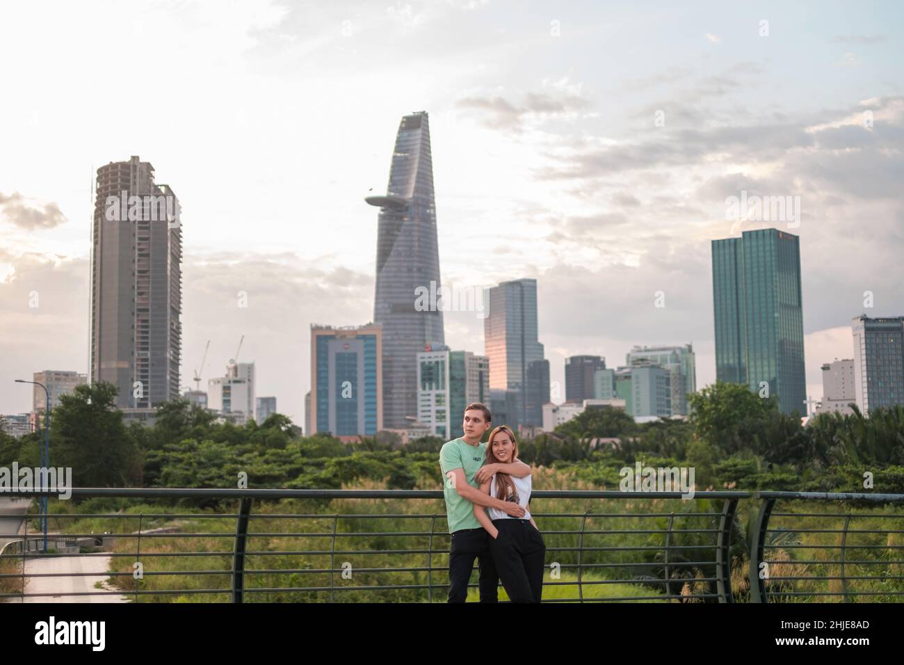 Bella coppia mista in piedi sul ponte nel parco in metropoli e coccole. Amore persone e concetto di felicità. Grattacieli sullo sfondo Foto Stock
