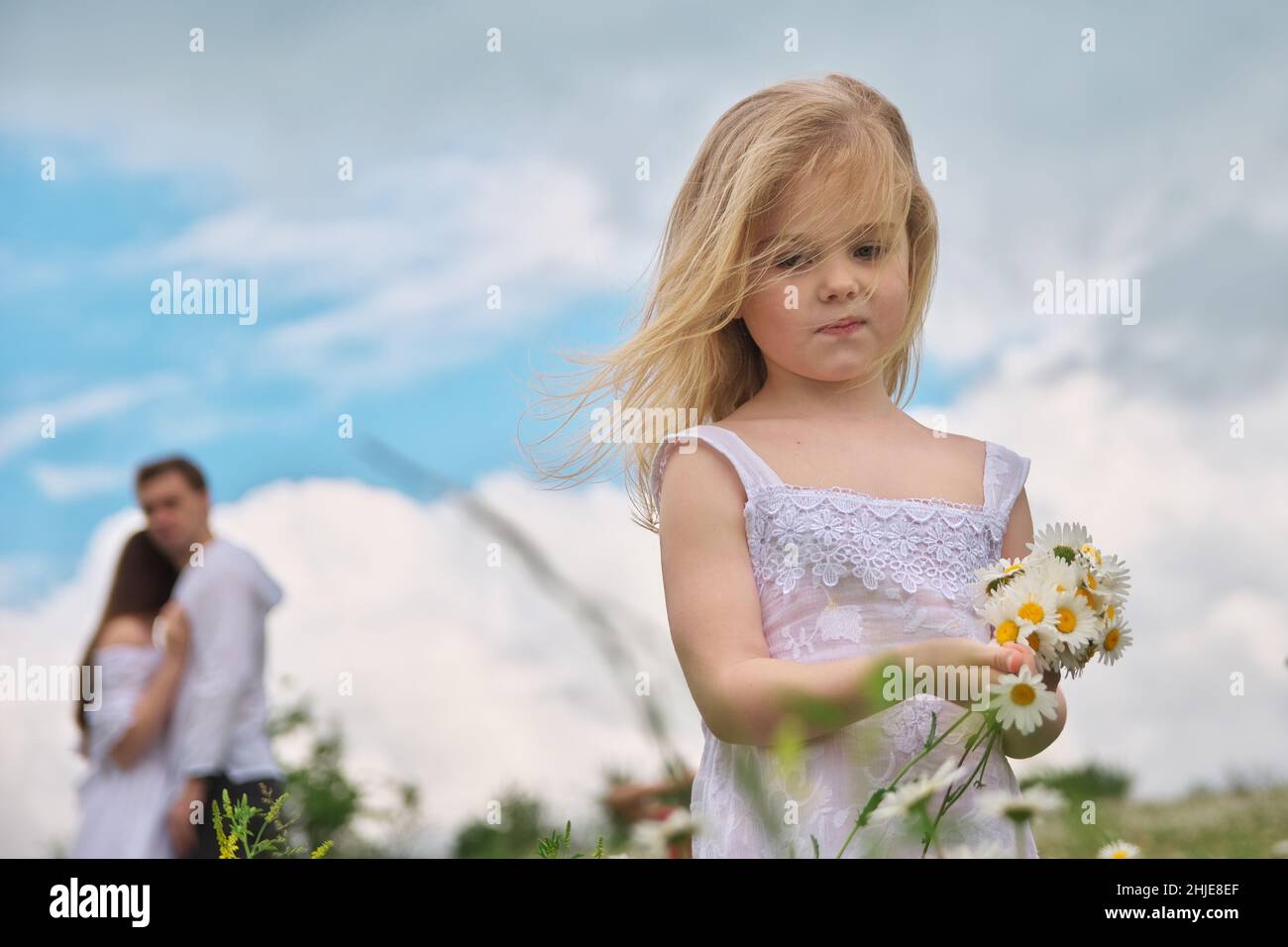 Bambina e i suoi genitori a sfondo blury su prato camomilla in natura. I bambini raccoliscono i fiori. Problema sociale e familiare. Foto Stock