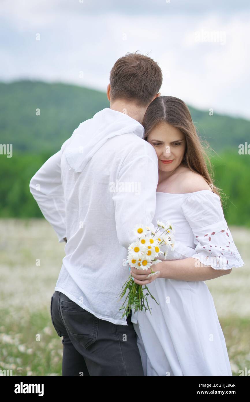 Coppia felice sul grande prato di montagna camomilla. Scena emozionale, d'amore e di cura. Foto Stock