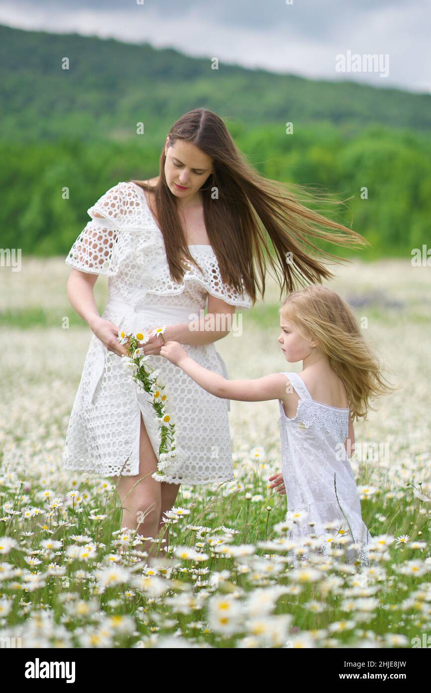 Felice madre e figlia che fanno corona in grande camomilla prato di montagna. Scena emozionale, d'amore e di cura. Foto Stock