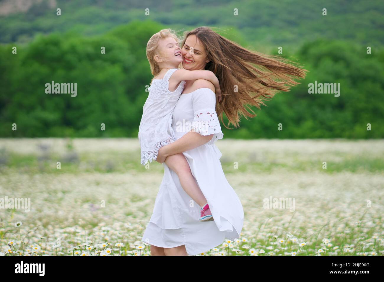Felice madre e figlia giocare in grande camomilla prato di montagna. Scena emozionale, d'amore e di cura. Foto Stock