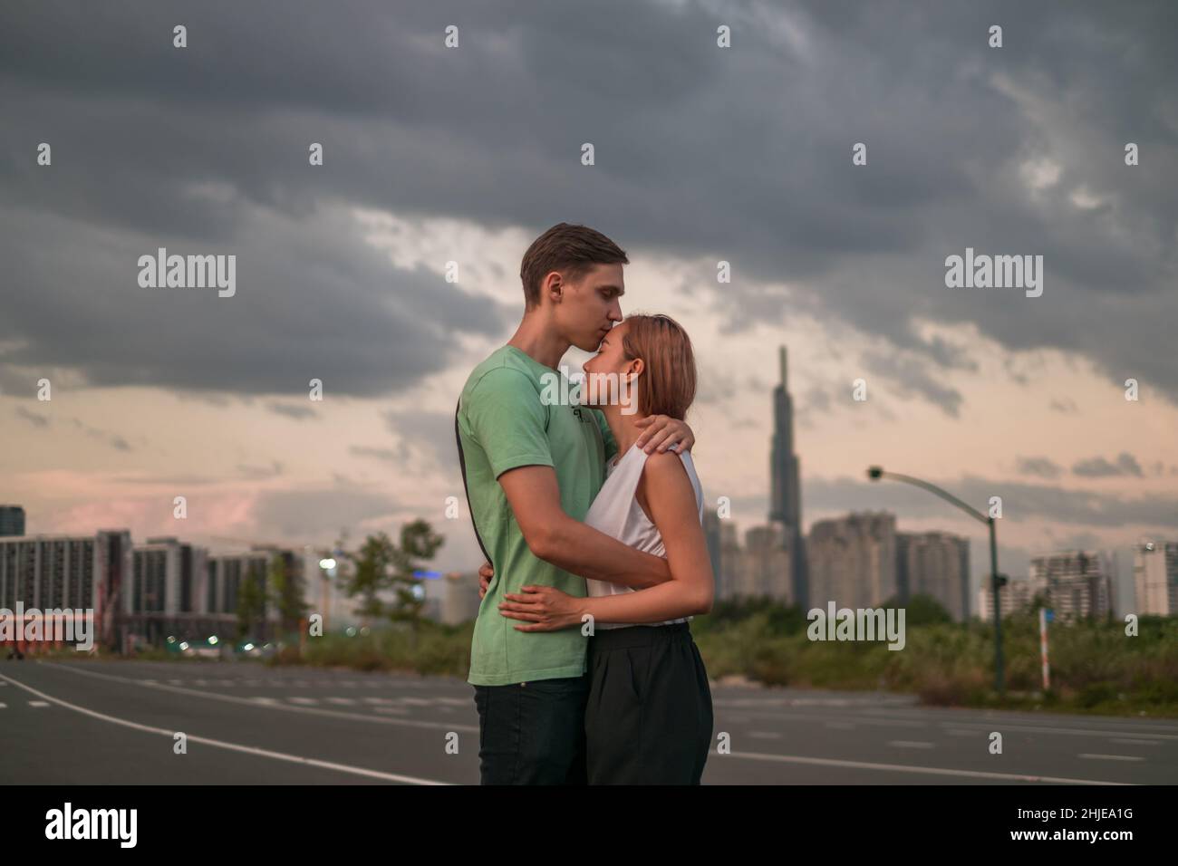 Bella giovane coppia in piedi sulla strada nella metropoli al tramonto e coccole. Il ragazzo bacia la ragazza. Grattacieli sullo sfondo Foto Stock