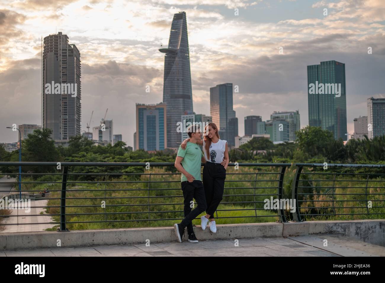 Bella coppia mista in piedi sul ponte nel parco in metropoli e coccole. Amore persone e concetto di felicità. Grattacieli sullo sfondo Foto Stock