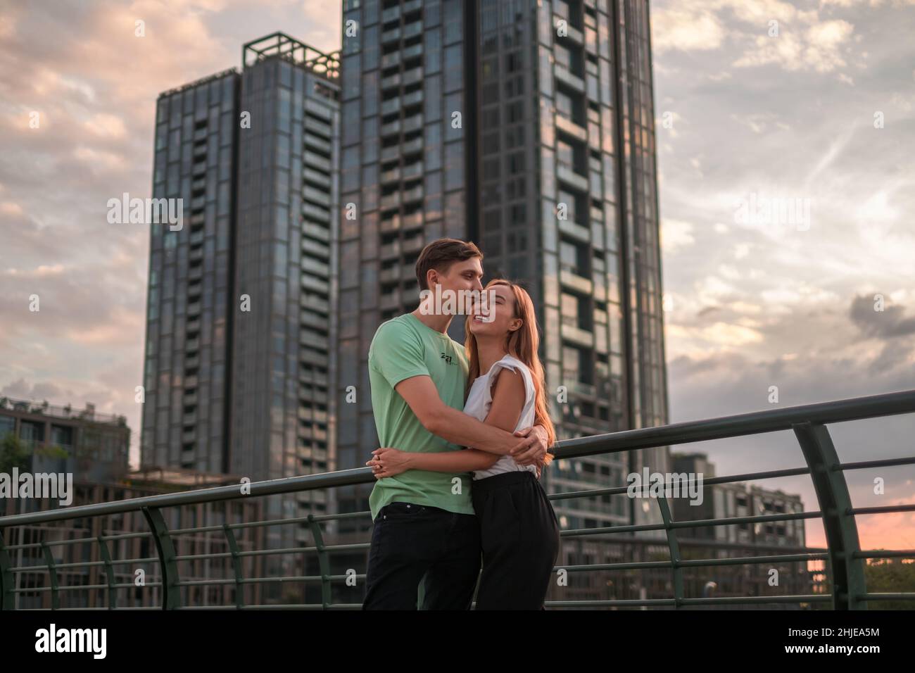 Bella giovane coppia in piedi sulla strada nella metropoli al tramonto e coccole. Il ragazzo bacia la ragazza. Grattacieli sullo sfondo Foto Stock