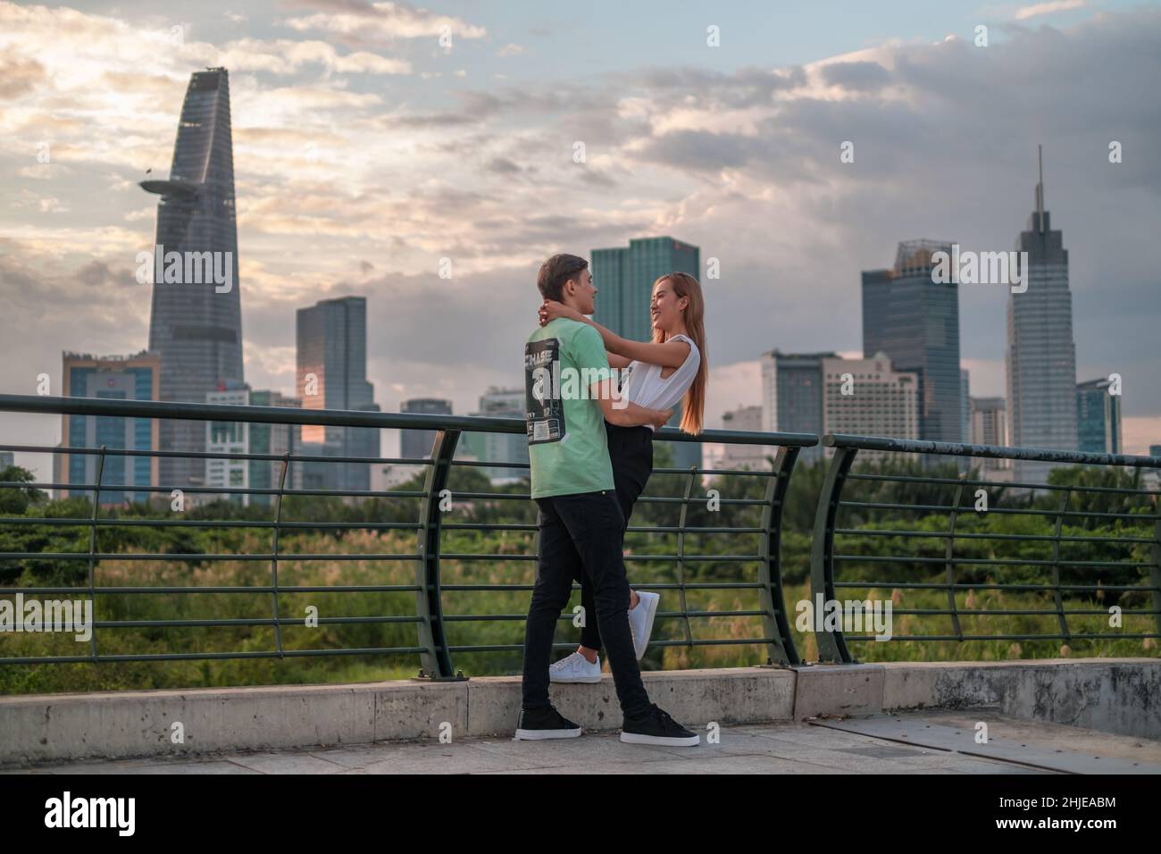Bella coppia mista in piedi sul ponte nel parco in metropoli e coccole. Amore persone e concetto di felicità. Grattacieli sullo sfondo Foto Stock