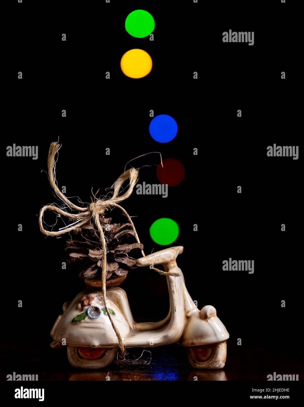 Un cono di pino legato con corda ad un modello scooter con luci colorate con effetto bokeh sullo sfondo Foto Stock