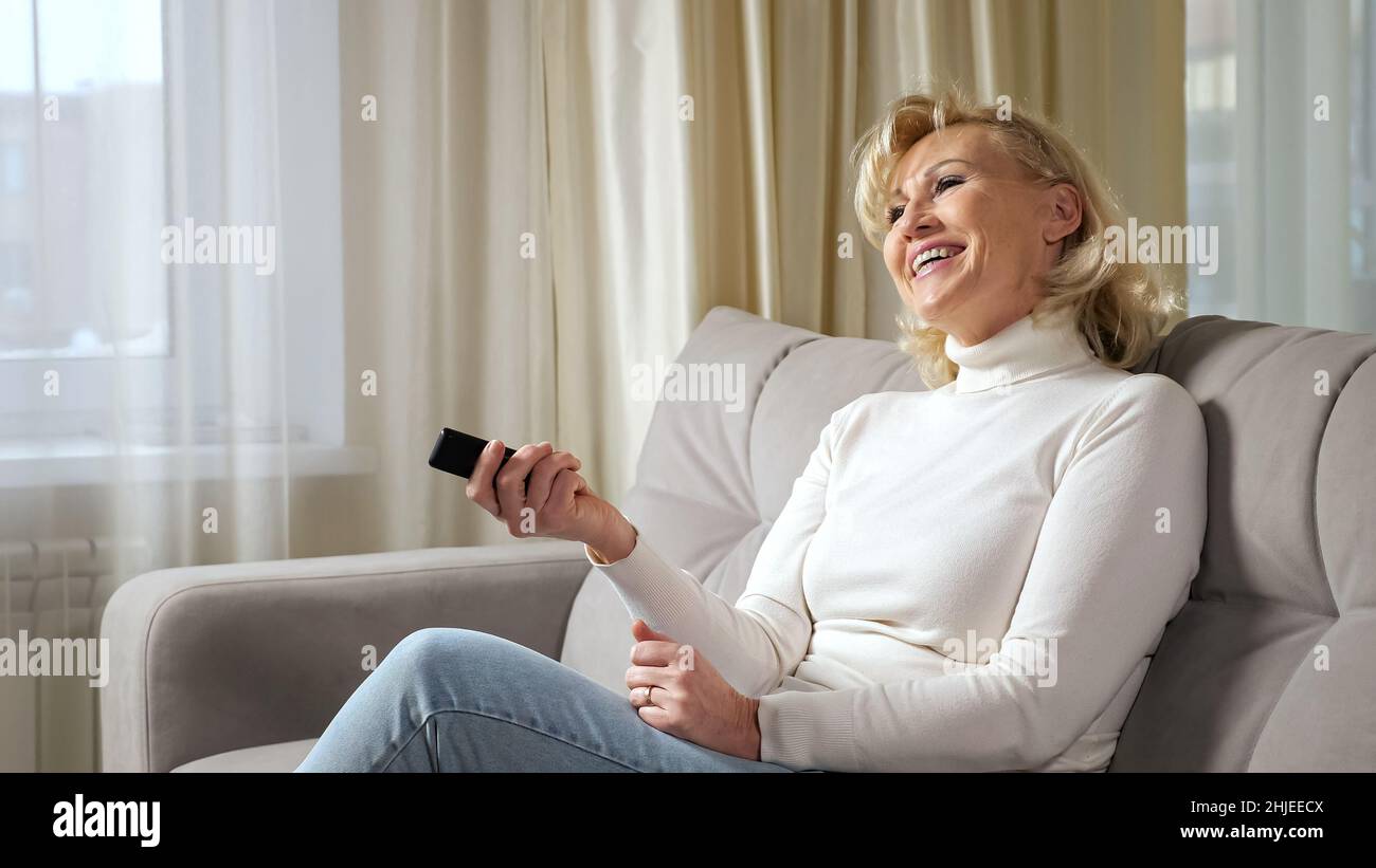 La donna bionda anziana ride e ama guardare la serie televisiva Foto Stock