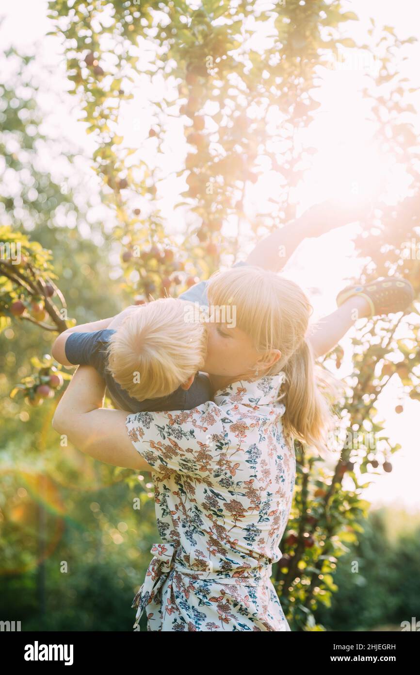 Giovane donna Madre abbracciare e scissare il suo bambino Figlio nel Giardino soleggiato. Ritratto estivo all'aperto Foto Stock