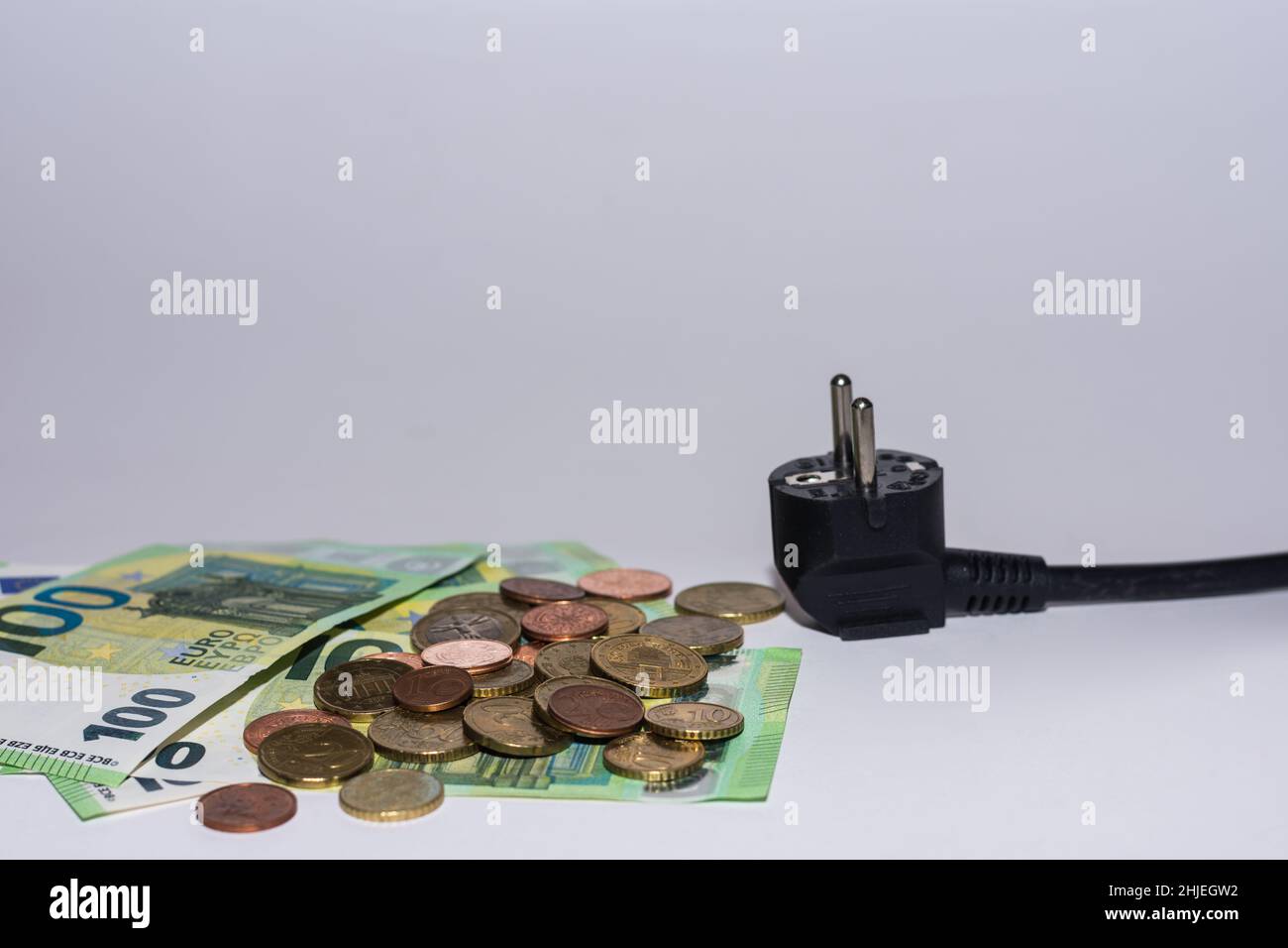 consumo di energia e aumento dei prezzi dell'elettricità molte banconote e monete in euro con una spina di alimentazione su sfondo grigio Foto Stock
