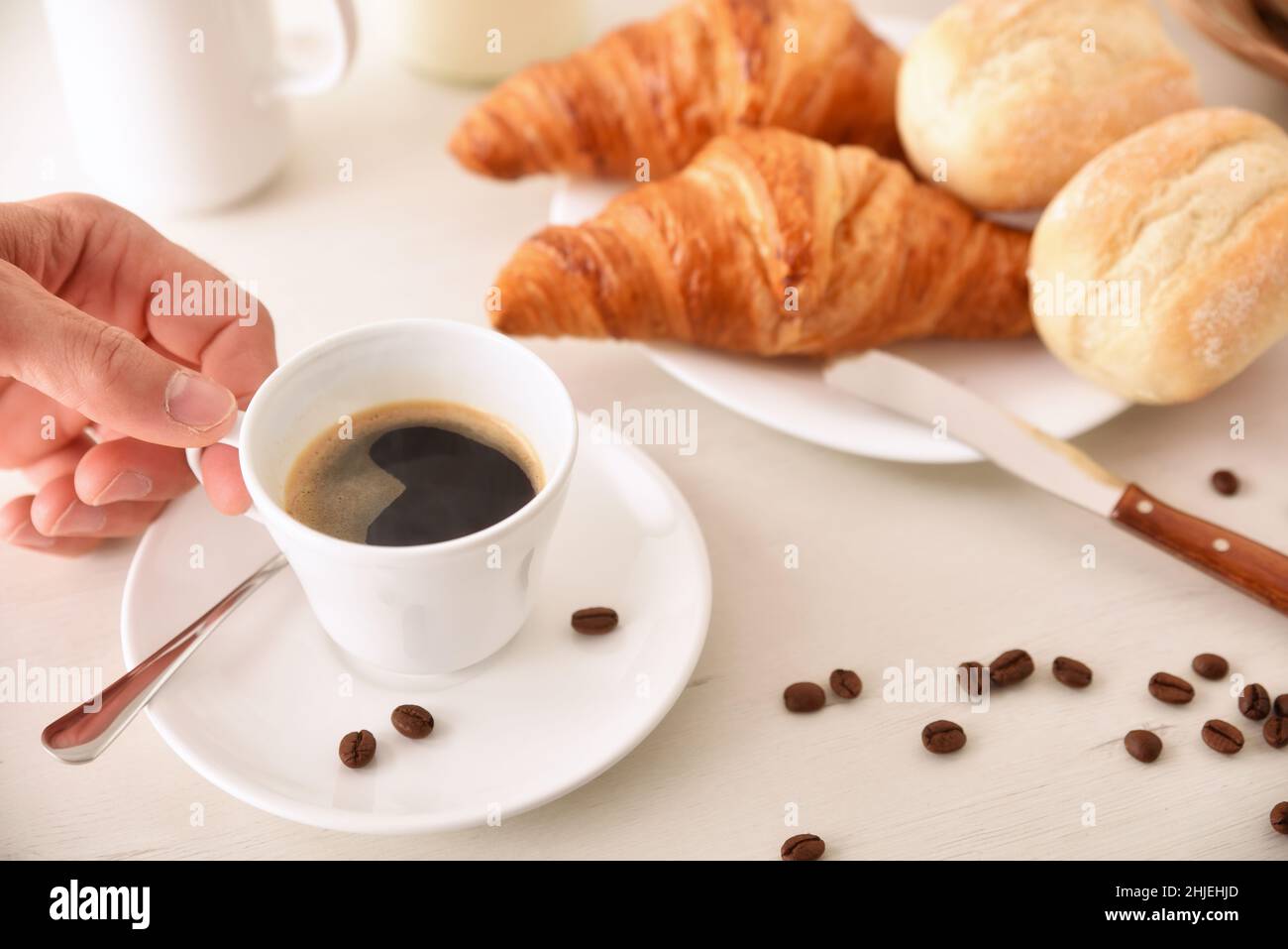 Al mattino, raccogliete una tazza di caffè caldo sul tavolo della colazione con croissant e panini. Vista rialzata. Composizione orizzontale. Foto Stock