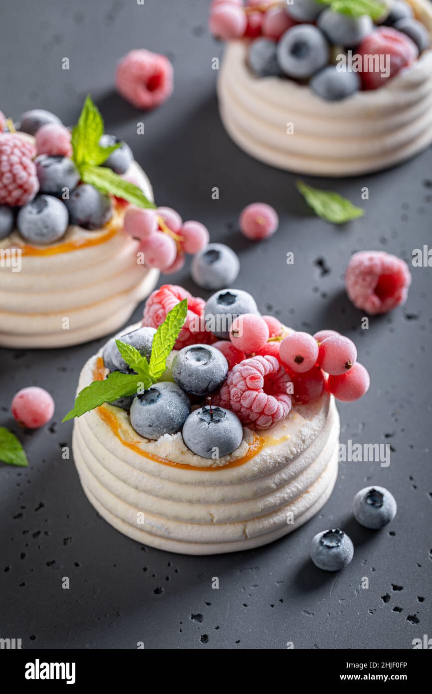 Mini dessert Pavlova cremoso con panna montata e frutta surgelata. Dessert Pavlova con lamponi congelati e mirtilli. Foto Stock