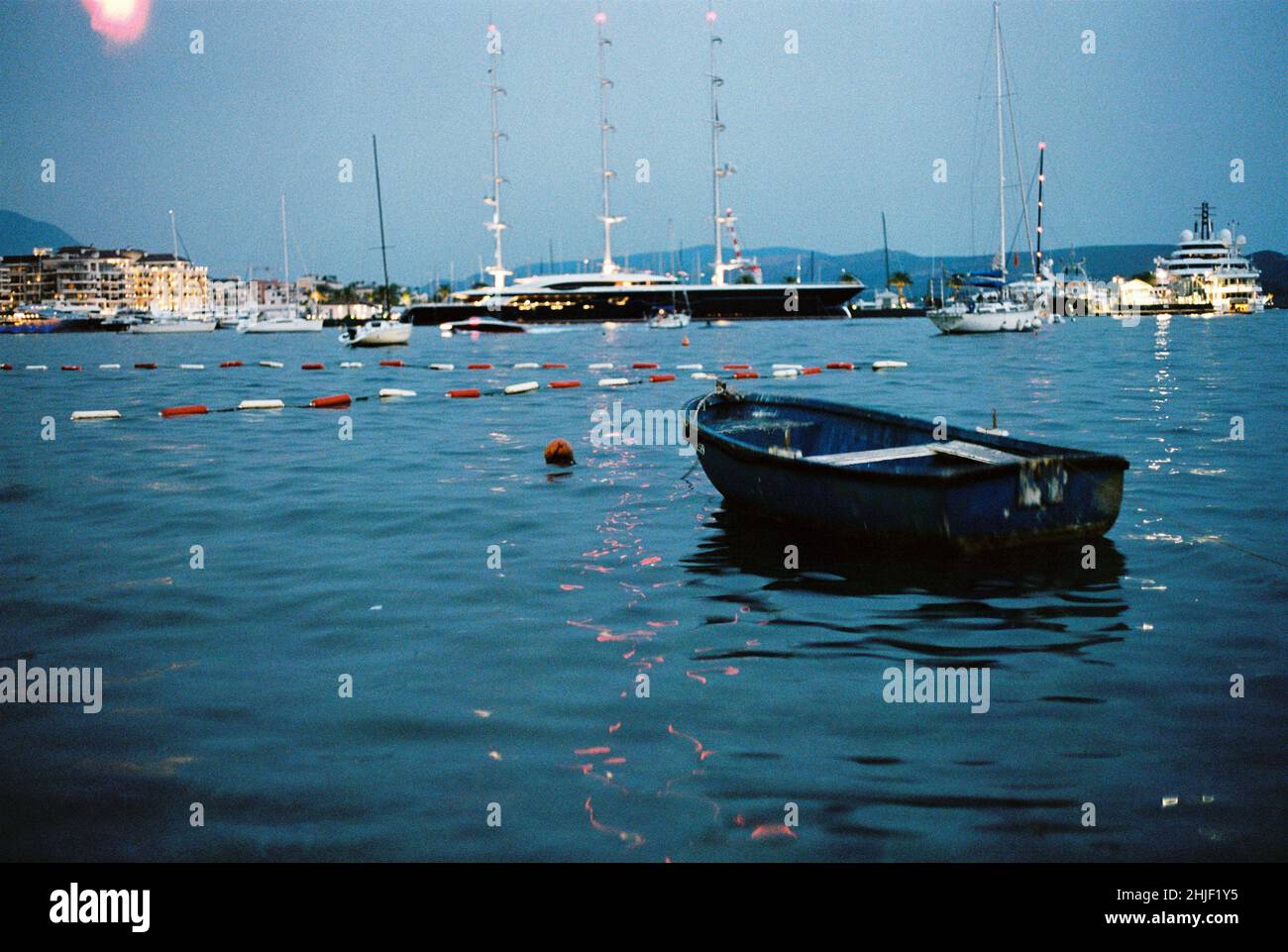 Piccola barca di pescatori blu solitaria arrugginita in piedi in mare, yacht costosi sullo sfondo Foto Stock