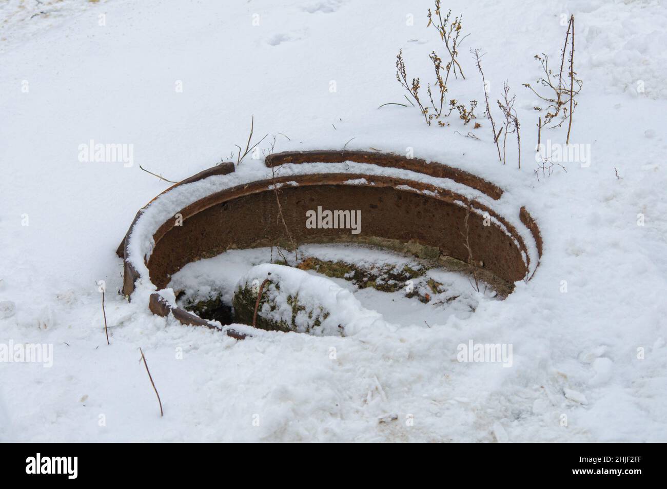 Aprire la botola fognaria con i rifiuti coperti di neve in inverno. Fognatura di emergenza pericolosa. Foto Stock
