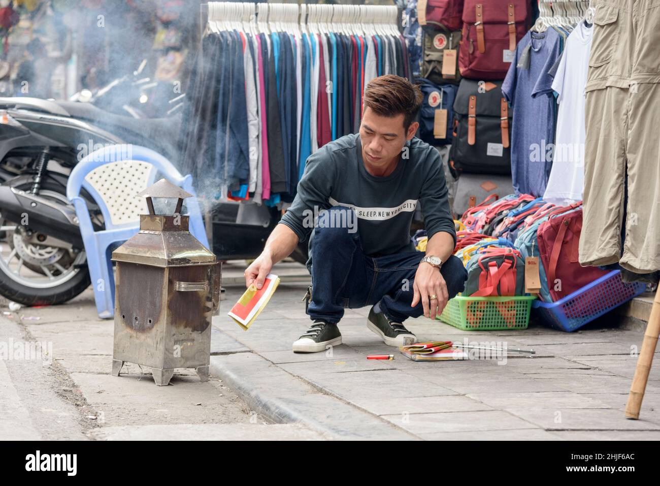 Un uomo vietnamita brucia denaro votivo (carta di scherzo, denaro falso, denaro di spirito) in un bruciatore per le strade del quartiere vecchio di Hanoi, Vietnam Foto Stock