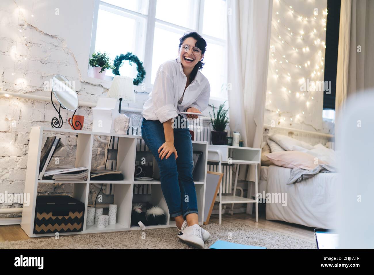 Donna sorridente in piedi vicino agli scaffali con smartphone Foto Stock