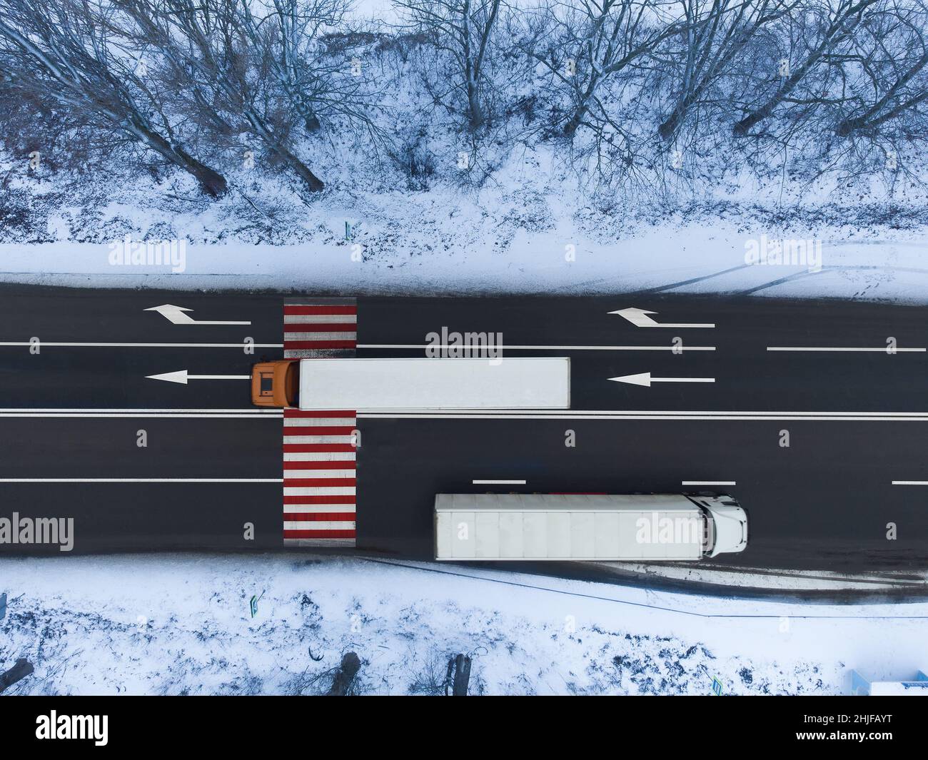 Due carrelli bianchi su strada vanno in direzioni diverse. Pericoloso attraversamento pedonale rosso e bianco sull'autostrada. Vista dall'alto della strada in inverno Foto Stock
