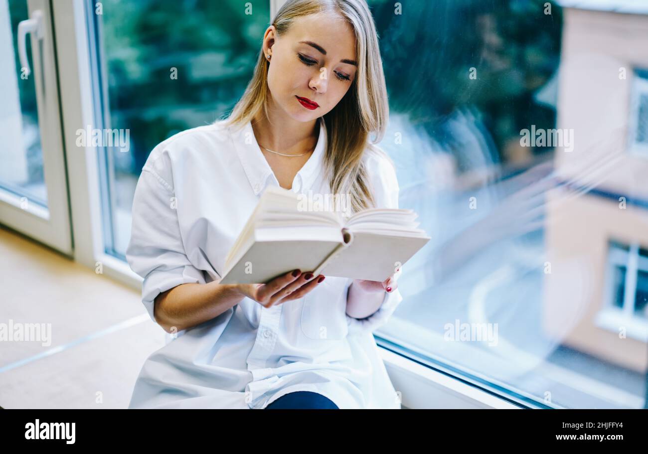 Donna focalizzata seduta su davanzale con libro Foto Stock