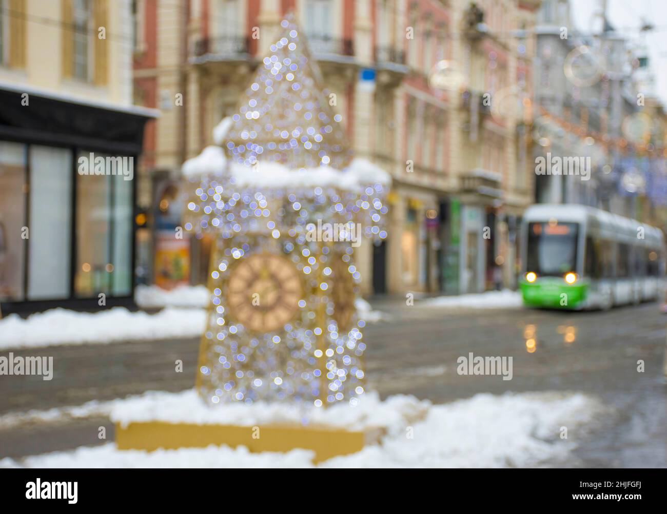 Luci di Natale sfocate con la famosa Torre dell'Orologio sulla via Herrengasse nel centro della città di Graz, Steiermark, Austria, in una giornata invernale nevosa. Foto Stock