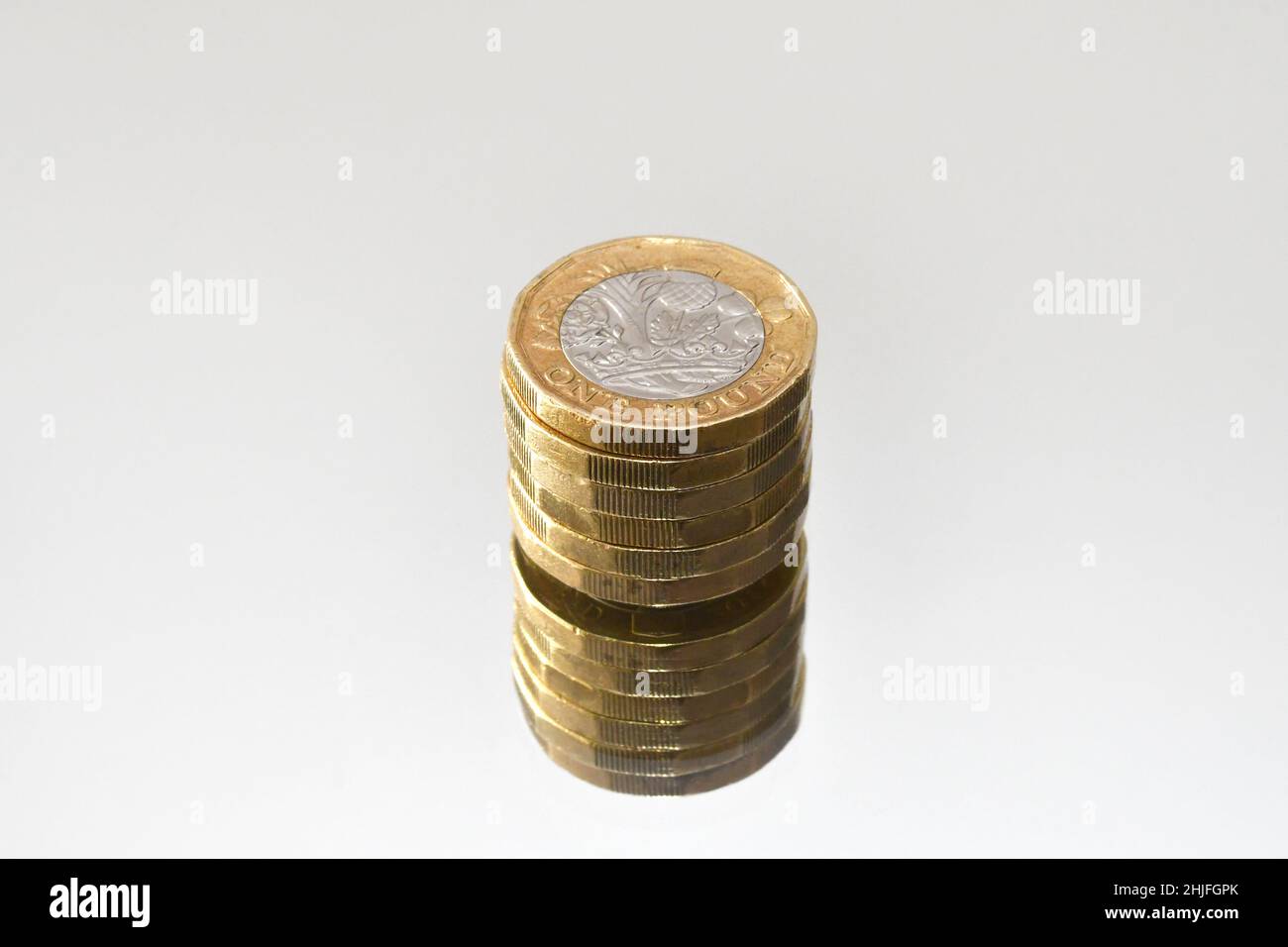 Primo piano di una colonna di monete da 1 libbra su come superficie a specchio isolato su un fondo bianco semplice. Nessuno. Spazio copia. Foto Stock