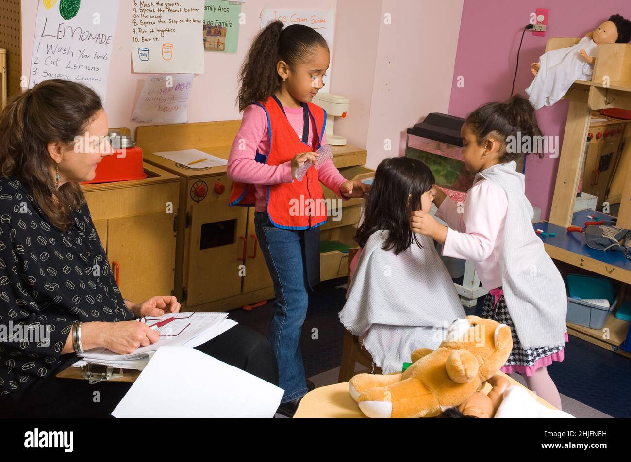 Istruzione Preschool classe 4-5 anni ricercatore che guarda gruppo di ragazze impegnate nel fingere di giocare parrucchiere, prendendo appunti Foto Stock