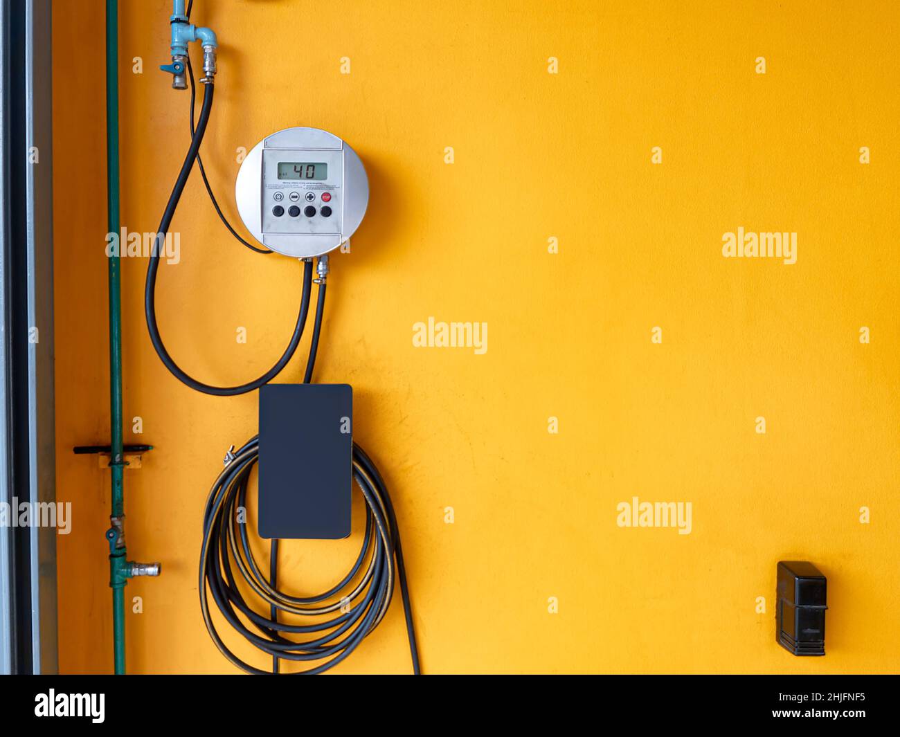 Kit del generatore di gas digitale del compressore con tubo in gomma appeso alla parete gialla nella stazione di servizio dell'auto Foto Stock