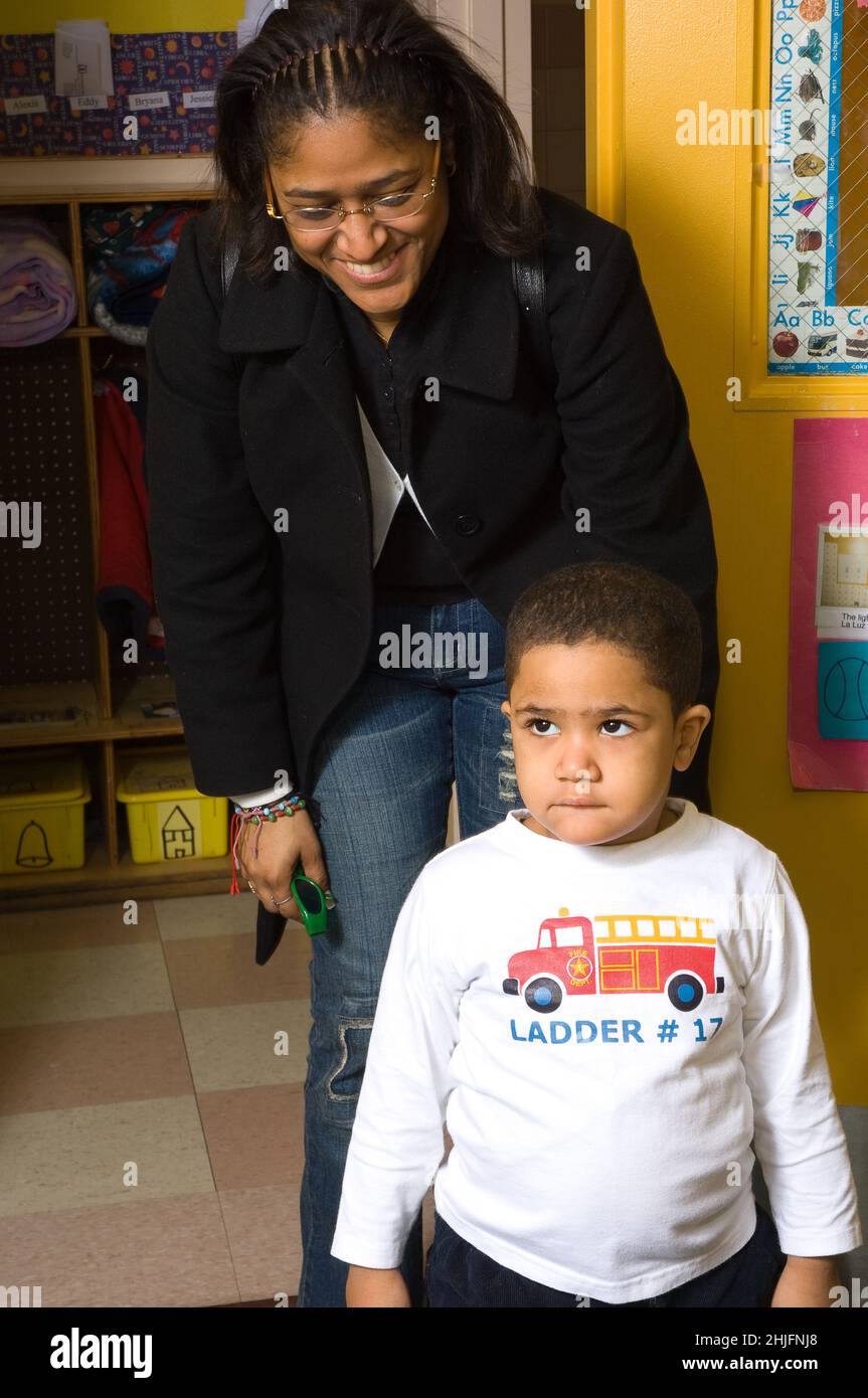 Istruzione prescolare classe età 3-4 ragazzo incerto che arriva in classe al mattino, sua madre dietro di lui Foto Stock