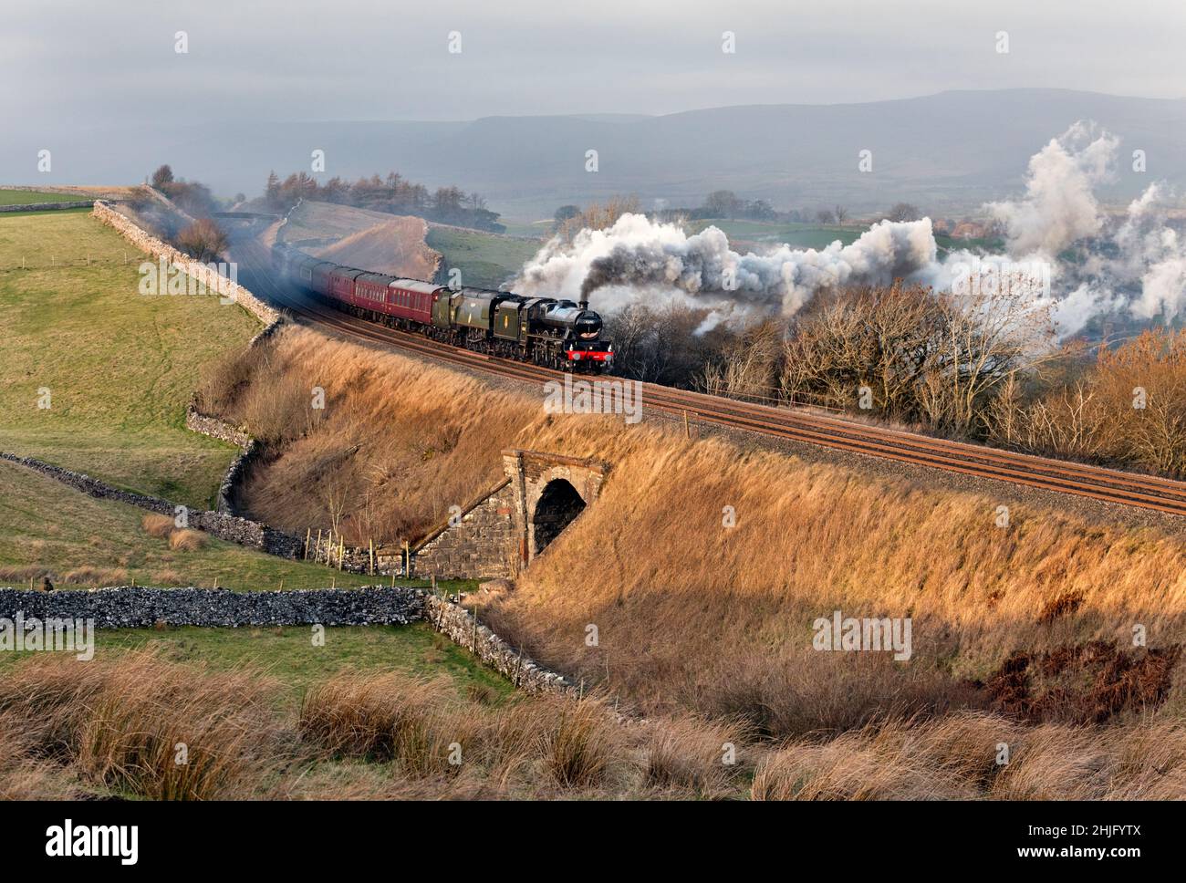 Kirkby Stephen, Cumbria, Regno Unito. 29th Jan 2022. Con un forte vento laterale, il "Winter Cumbrian Mountain Express" sale sul ripido pendio oltre Birkett Common, vicino a Kirkby Stephen, nel viaggio di ritorno a Preston. Forti venti diffondono il fumo dalle locomotive. Lo speciale Steam ha portato i passeggeri in un viaggio da Preston a Carlisle attraverso la linea principale della costa occidentale Shap e poi da Carlisle di ritorno a Preston attraverso la linea Settle-Carlisle, come si vede qui. La speciale era un raro treno a doppia testa, trainato da due locomotive a vapore 'Leander' e 'Tangmere'. Credit: John Bentley/Alamy Live News Foto Stock