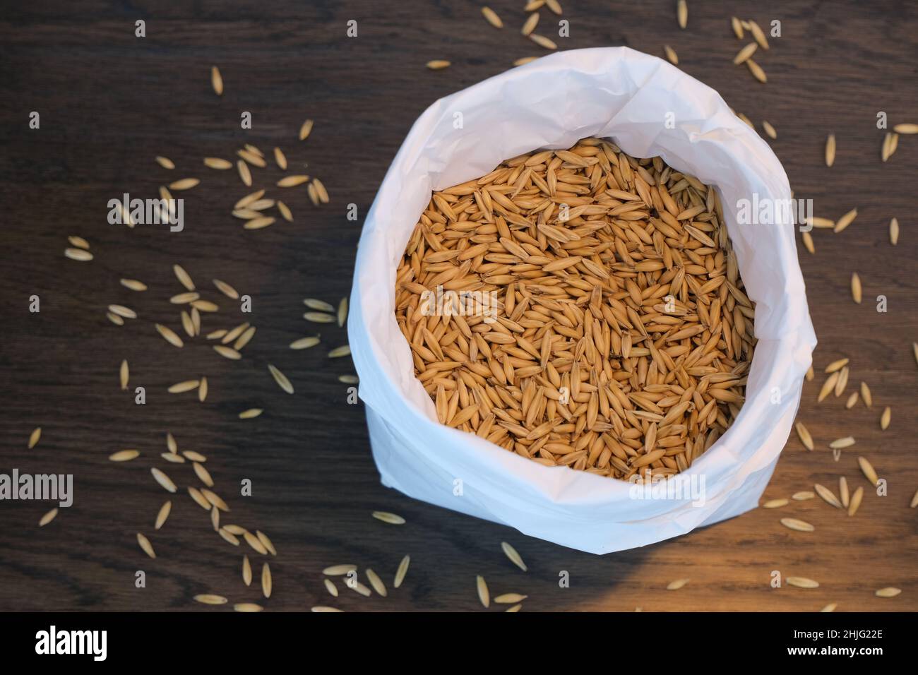 Sacco di carta bianca con 1 kg di avena, semi su tavola di legno scuro in luce calda, fotografato direttamente dall'alto Foto Stock