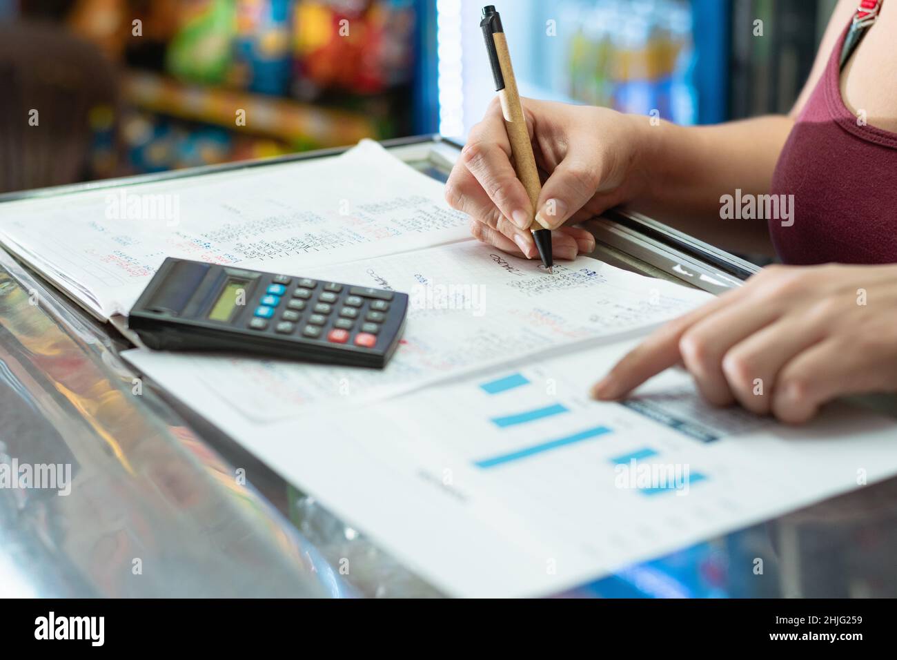 latina donna che punta al suo grafico delle statistiche di affari, mentre scrive con la sua altra mano su un grande taccuino con la sua penna ecologica di cartone, machina Foto Stock