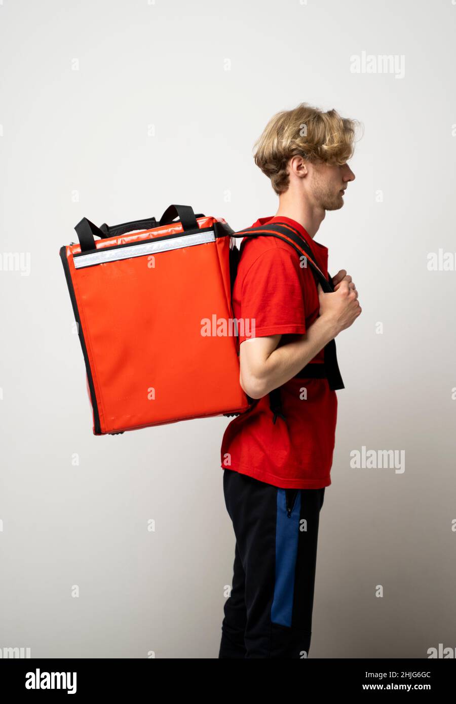 Concetto di servizio Fast Food Delivery. Vista laterale del corriere  maschio sorridente che indossa uniforme rossa e che tiene la borsa termica  zaino isolato in studio Foto stock - Alamy