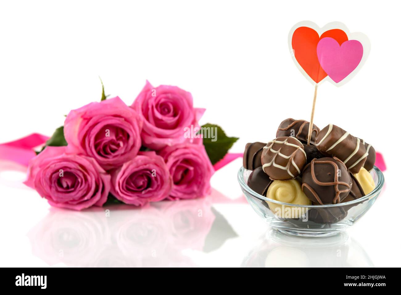 Praline di cioccolato in recipiente di vetro e bouquet di rose rosa su sfondo bianco. San Valentino e Womens Day concetto, fuoco selettivo. Foto Stock