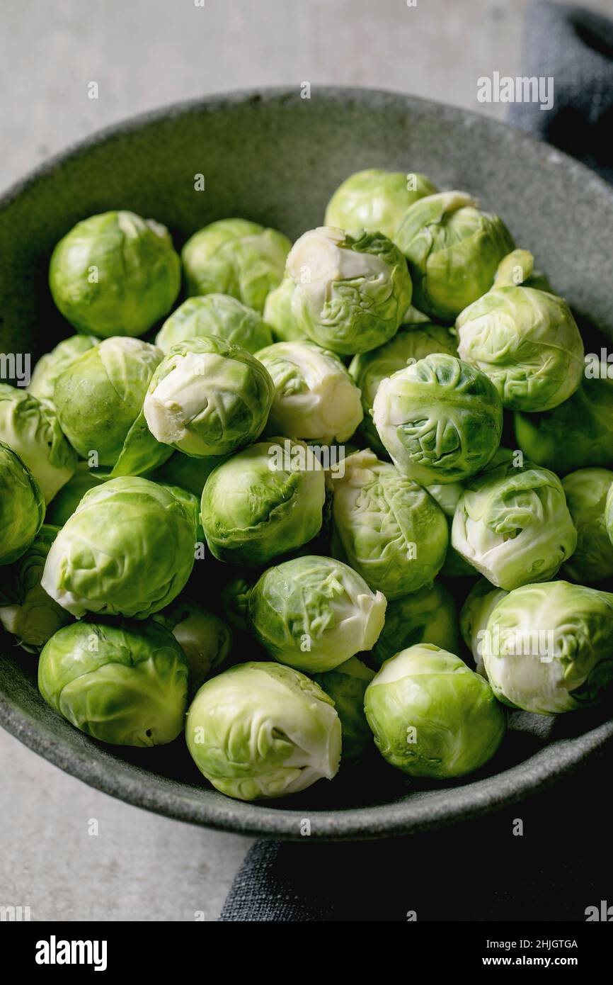 Mucchio di germogli biologici crudi bruxelles pelati mini cavolo in ciotola di ceramica su sfondo grigio chiaro. Verdure mangiare sano. Foto Stock