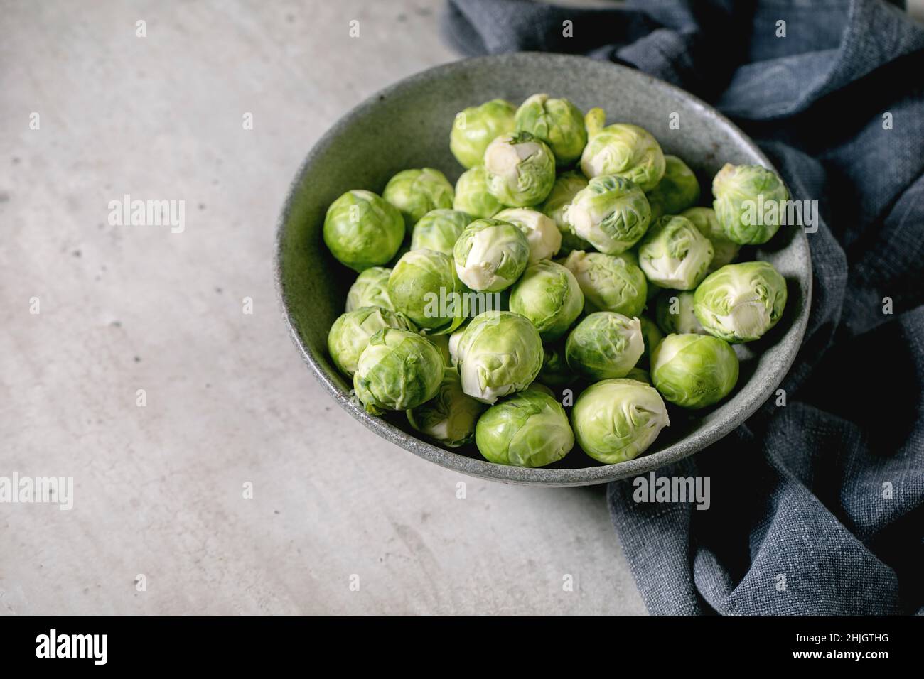 Mucchio di germogli biologici crudi bruxelles pelati mini cavolo in ciotola di ceramica su sfondo grigio chiaro. Verdure mangiare sano. Spazio di copia Foto Stock