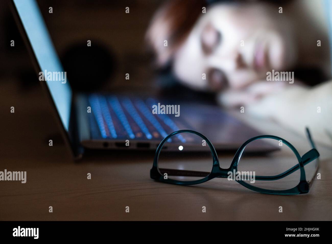 Donna stanca che dorme sul posto di lavoro vicino al laptop. Ragazza si è staccata per lavoro remoto. Lo studente sovraccarico si addormentò sul tavolo. Occhiali in primo piano. Foto Stock