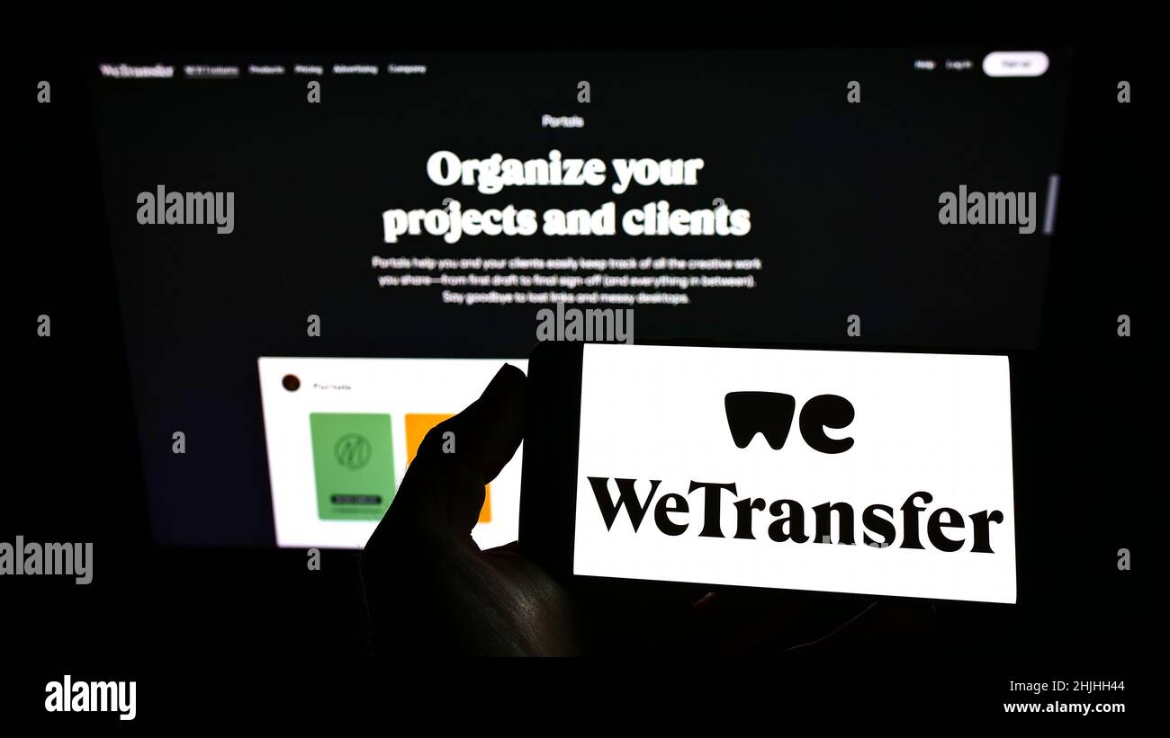 Persona che tiene uno smartphone con il logo della società olandese WeTransfer B.V. sullo schermo di fronte al sito web. Mettere a fuoco sul display del telefono. Foto Stock
